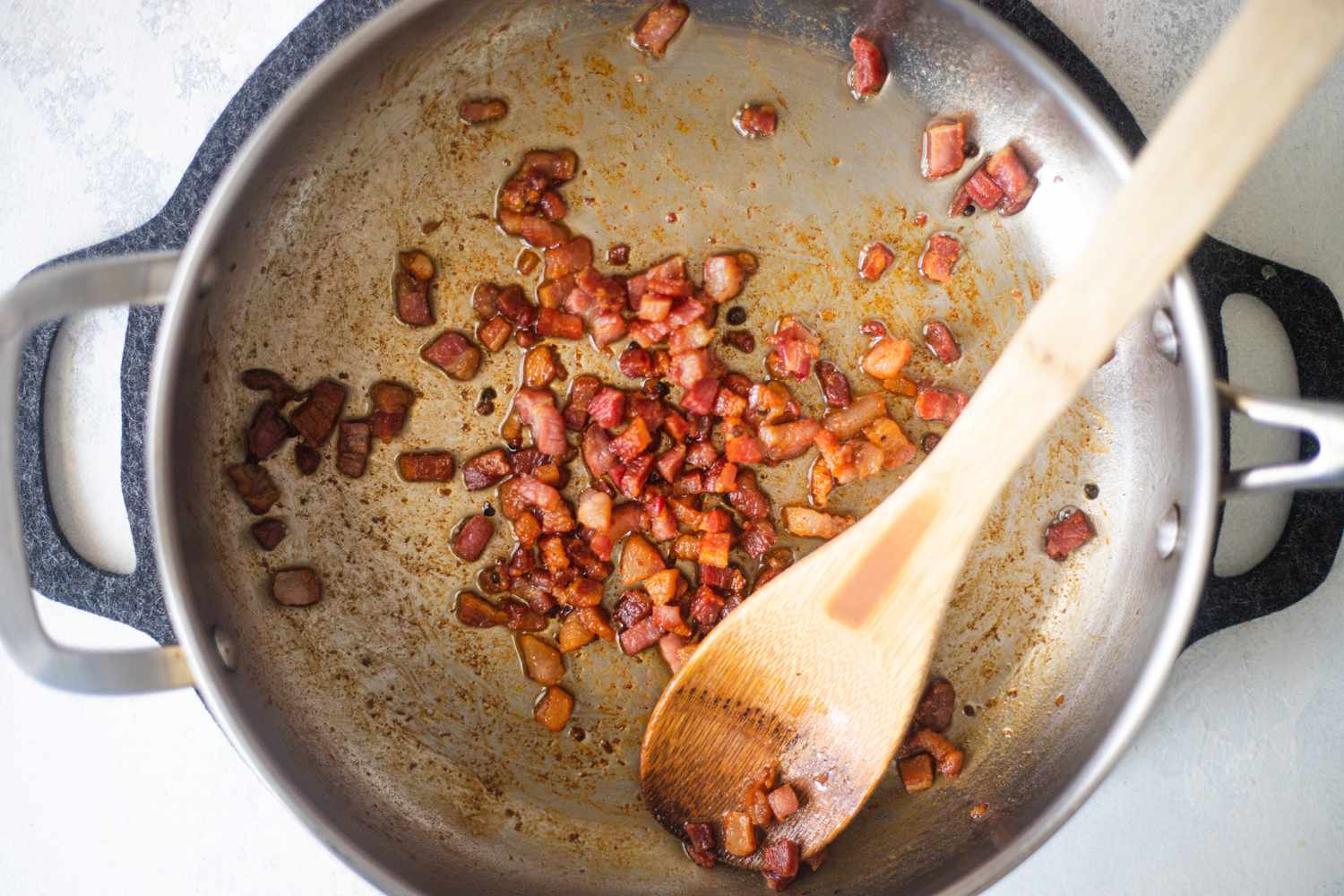A skillet with chopped bacon and a wooden spoon to make Spaghetti Carbonara.