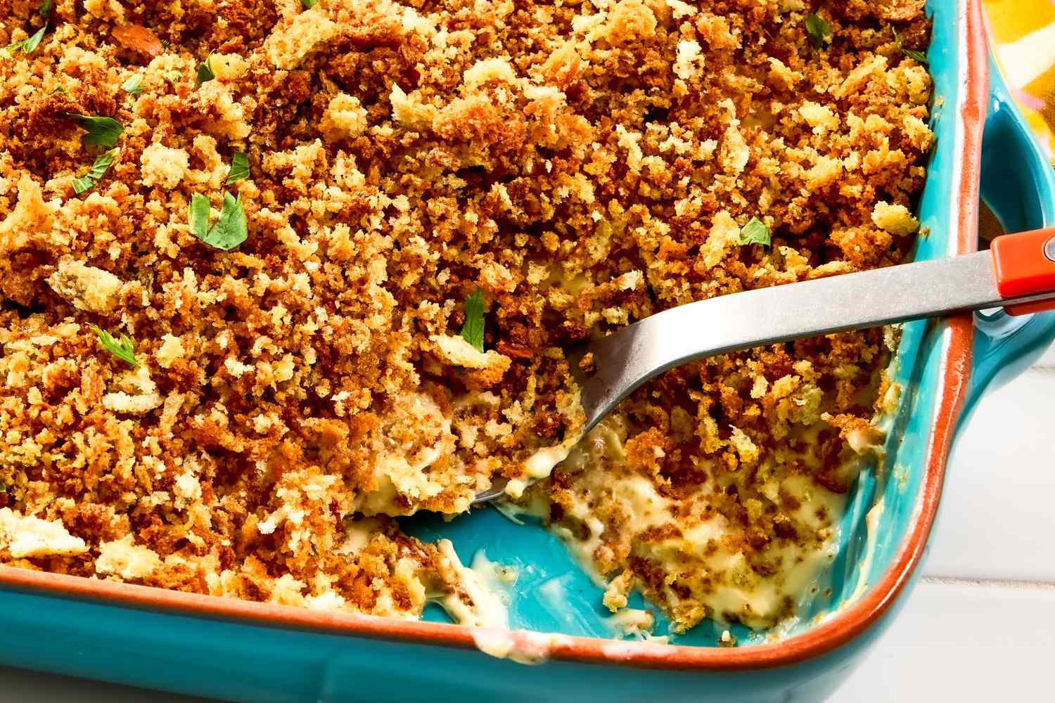 Casserole with a bread crumb topping in a blue dish a serving spoon scooping portion out
