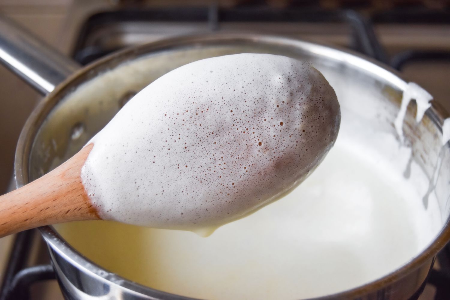 A wooden spoon coated in eggnog with a pot of eggnog in the background