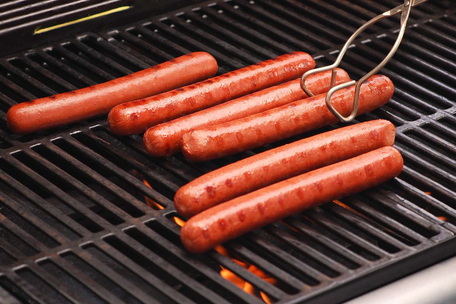 Hot dogs grilling on a barbecue with flames below