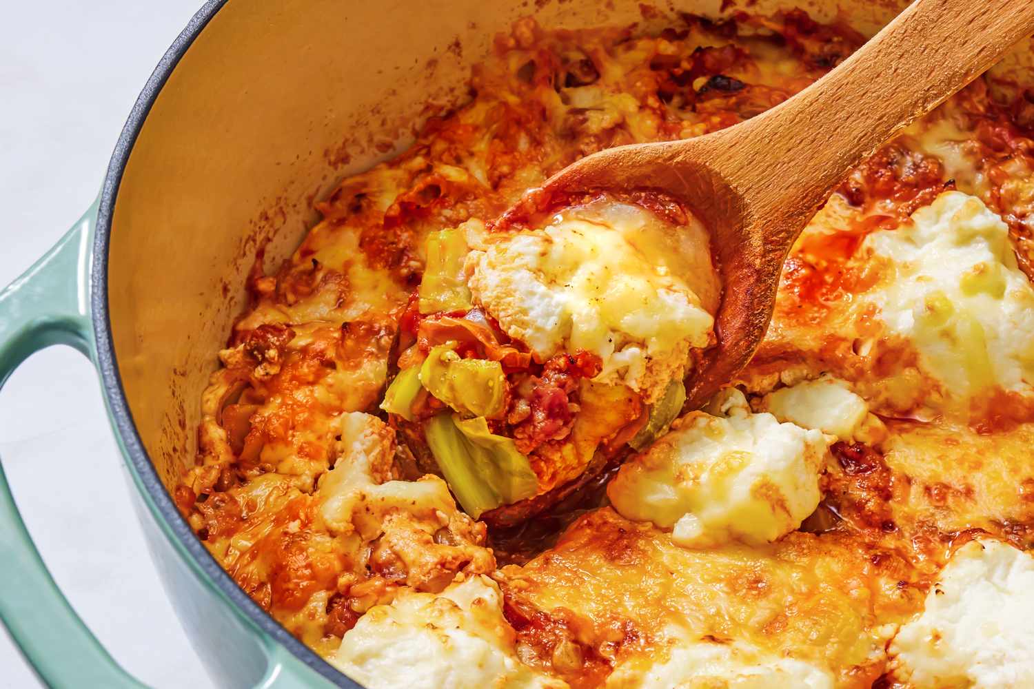 Cooked lasagna with layers of cheese and cabbage in a pot served with a wooden spoon