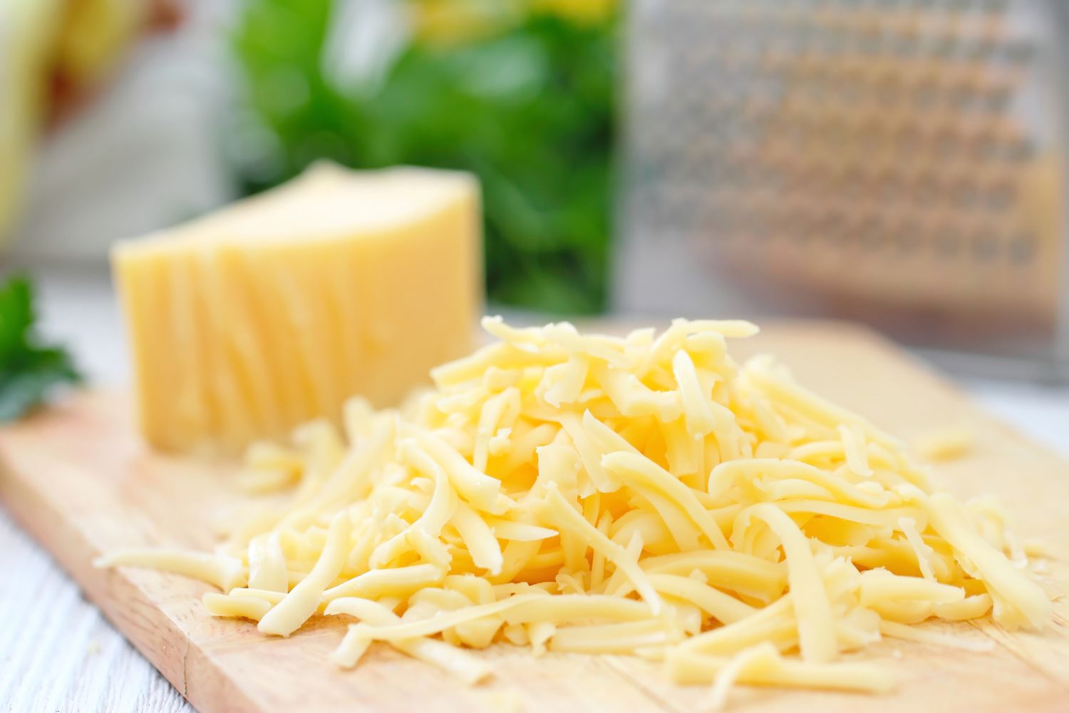 Grated cheese and a wedge of cheese on a wooden cutting board near a grater