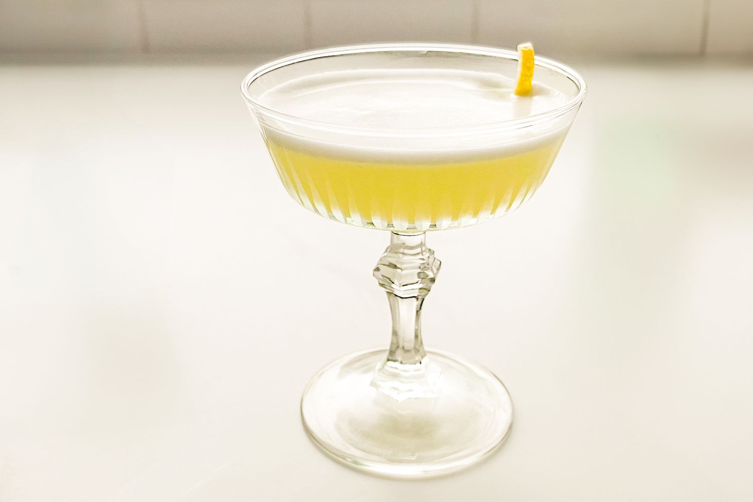 Stemmed glass containing a yellow cocktail with a garnish twist on top