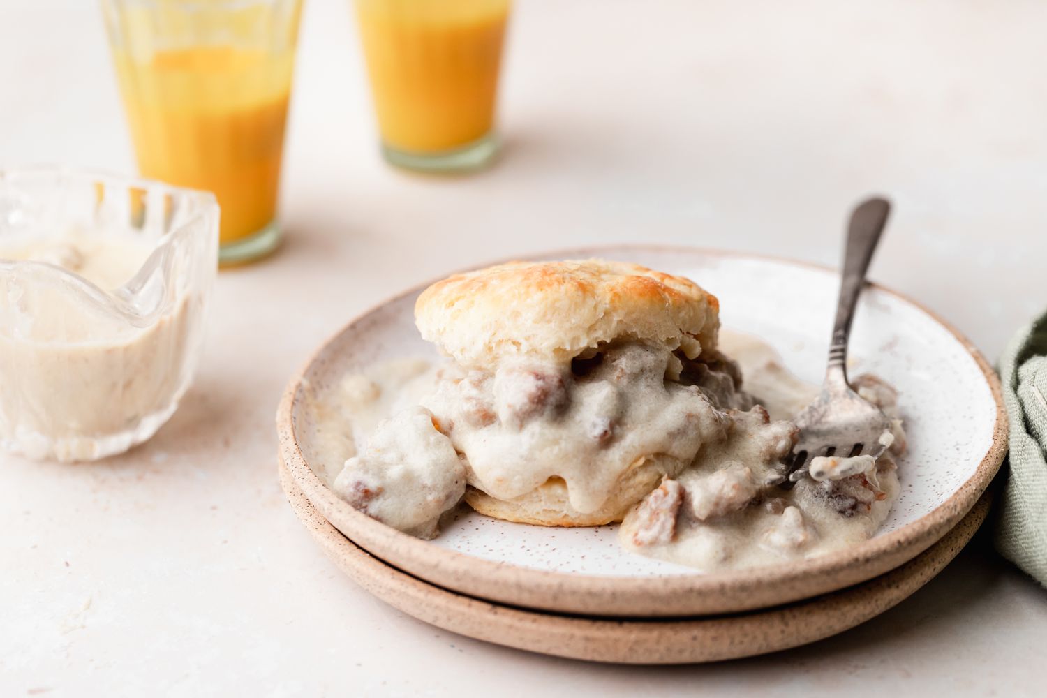 Biscuits and gravy on a plate with orange juice behind it.