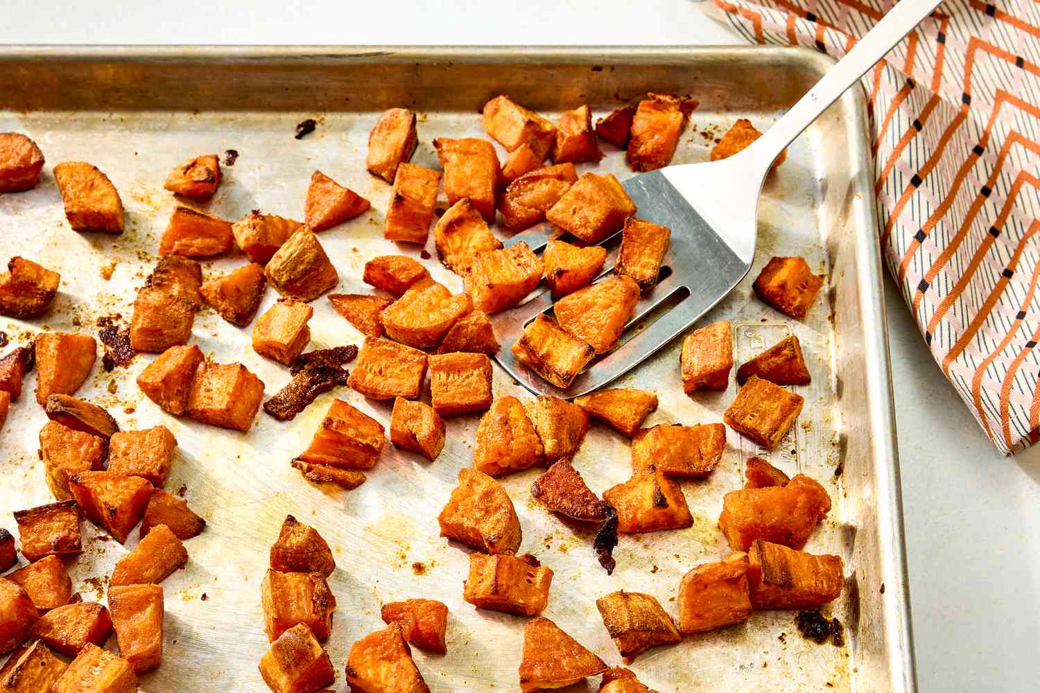 Overhead view of a baking sheet with cubes of roasted sweet potato along with a metal spatula