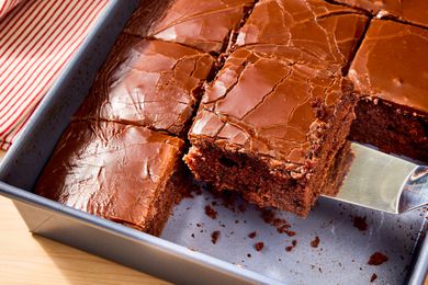 Metal baking pan of sliced coca cola cake with a slice being removed with a metal spatula