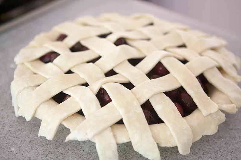 Unbaked homemade cherry pie on a counter and filled with cherry pie filling. A lattice top crust is constructed over the sweet cherries.