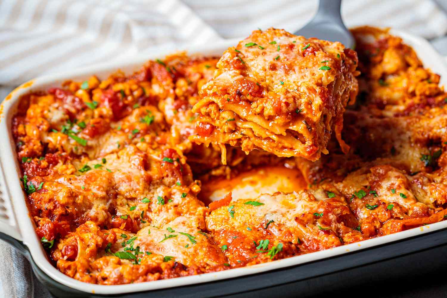 A baked lasagna tray with a portion being lifted out with a spatula layers of pasta cheese and meat visible
