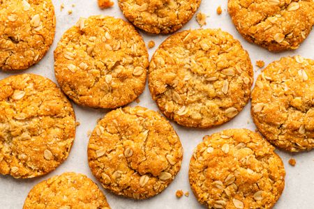 anzac biscuits laid out on a white surface, with some cookie crumbs surrounding them