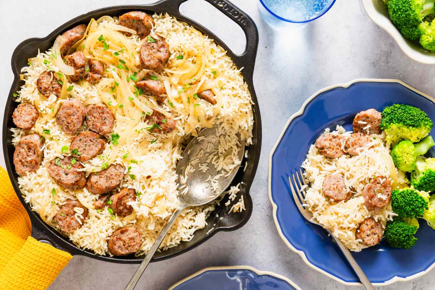 A skillet with sausage and rice dish a serving plated alongside with broccoli