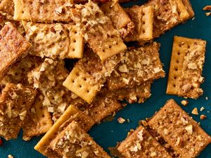 A pile of club crackers topped with crushed nuts on a teal background