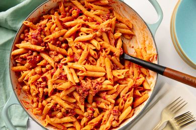 Chickpea pasta in tomato-based sauce served in a pot, with a serving spoon and nearby place settings