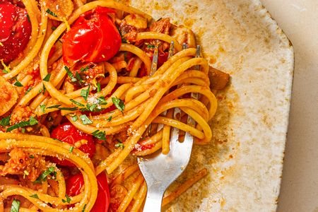 Spaghetti served with cherry tomatoes and herbs a fork is placed on the plate