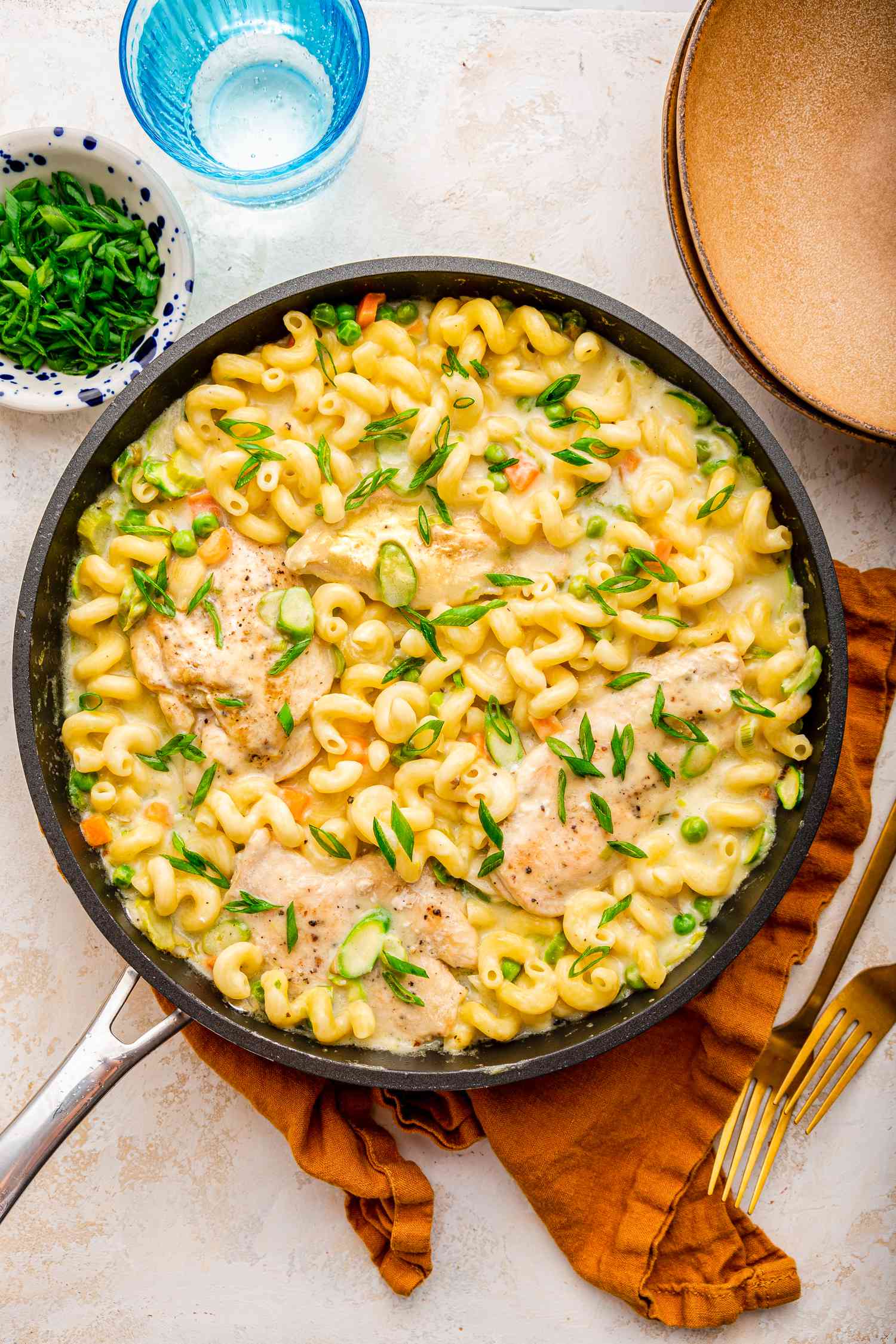 easy chicken primavera at a table setting with a bowl of sliced green onions, a bowl, and utensils on the counter