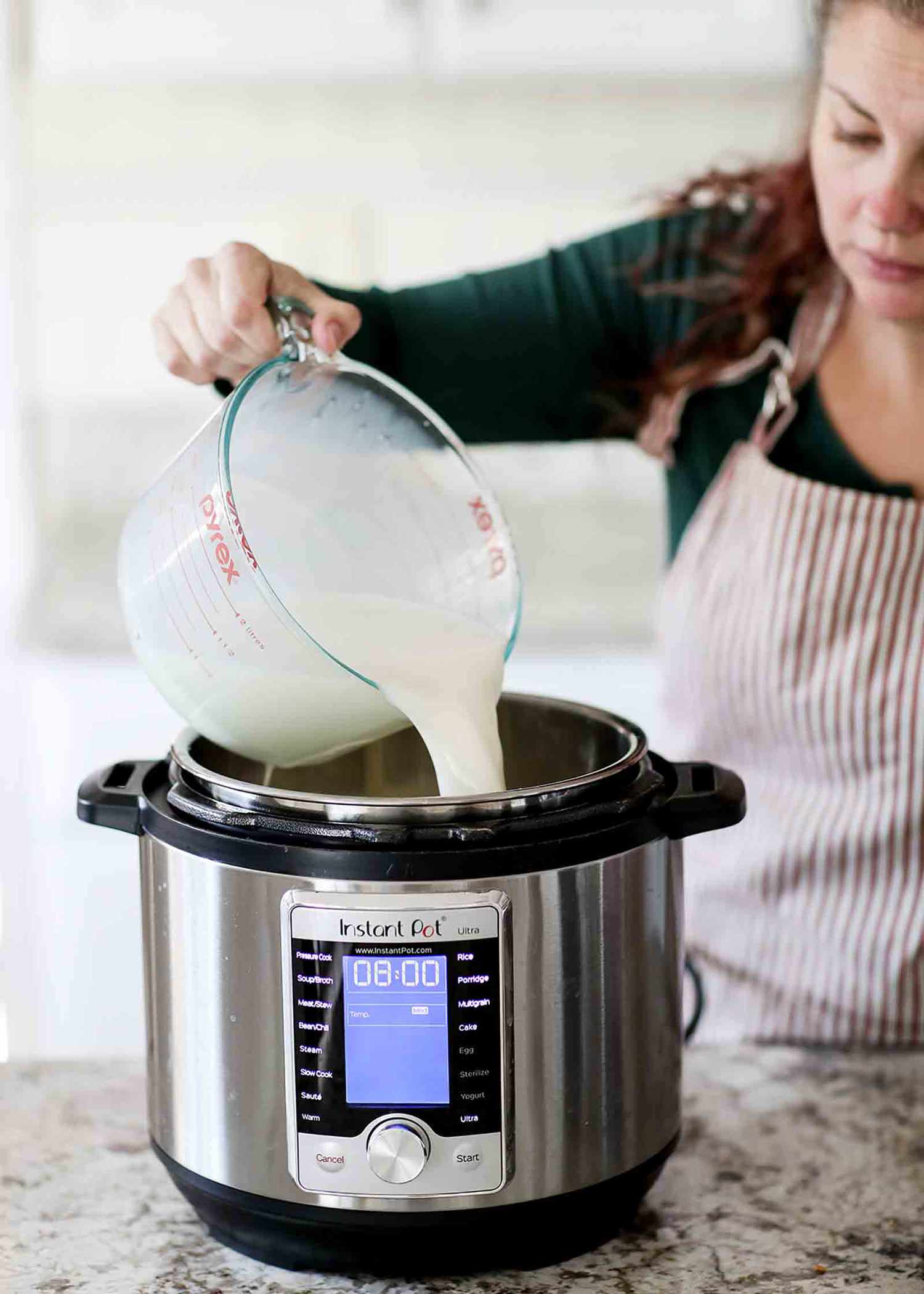 Yogurt mixture being poured from a large measuring glass into a Pressure Cooker