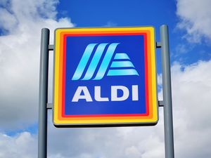 An Aldi supermarket sign mounted on poles against a cloudy sky