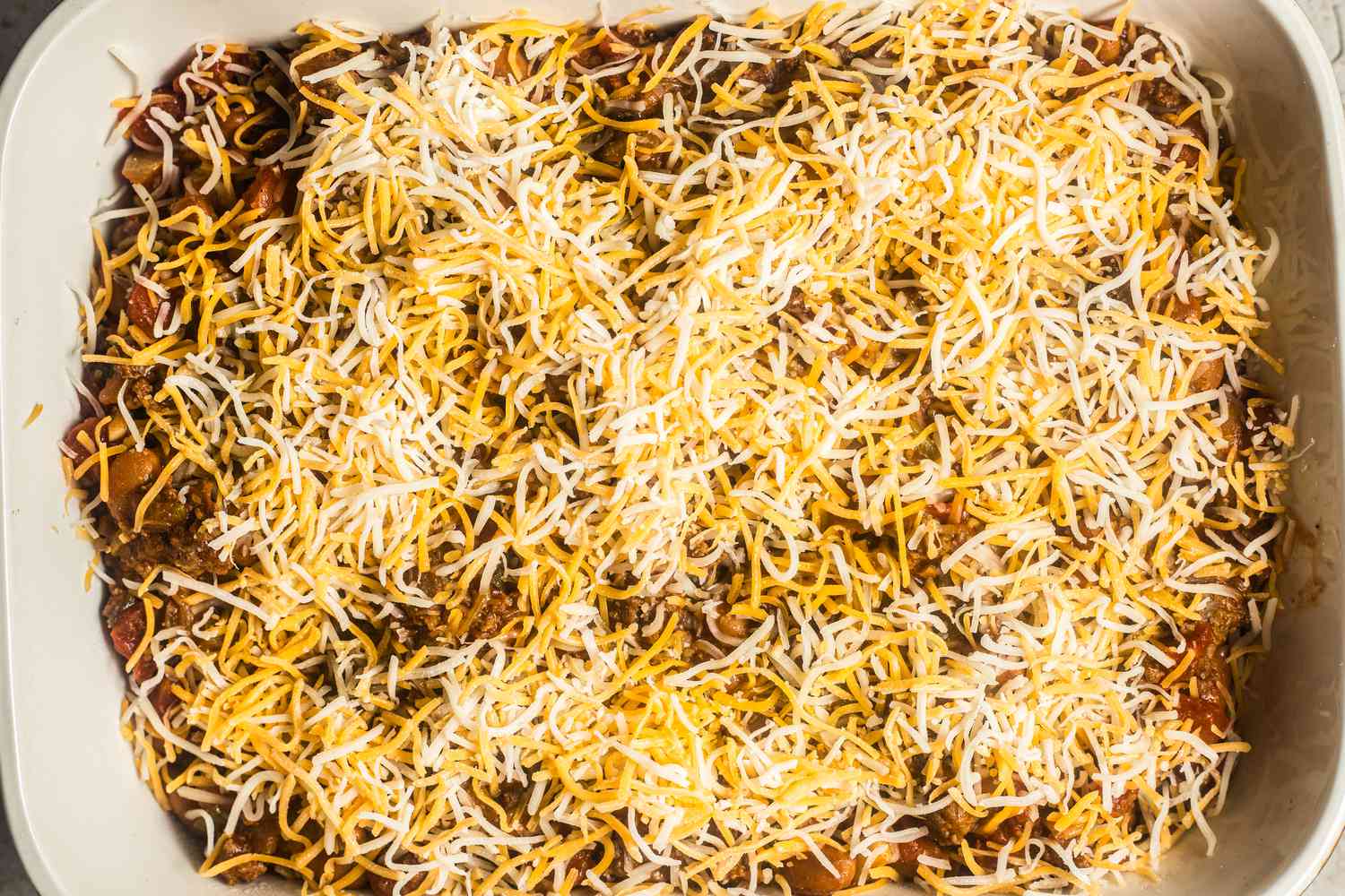 Walking taco casserole filling in a casserole dish and topped with shredded cheese