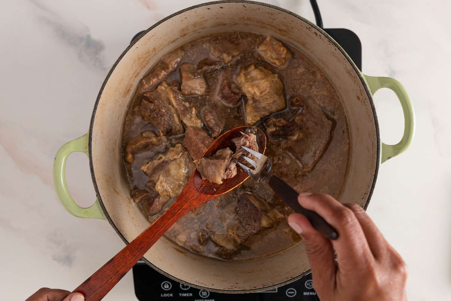 Checking for fork tender beef after lifing some from Dutch oven using a wooden spoon, and below it, the Dutch oven with the rest of the beef for Filipino beef stew recipe