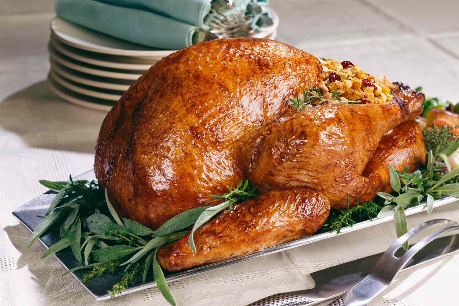 A whole roasted turkey on a serving plate, with herbs around it as decoration