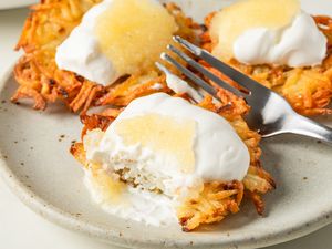 Plate of prepared latkes topped with sour cream and applesauce displaying a fork and partially eaten piece