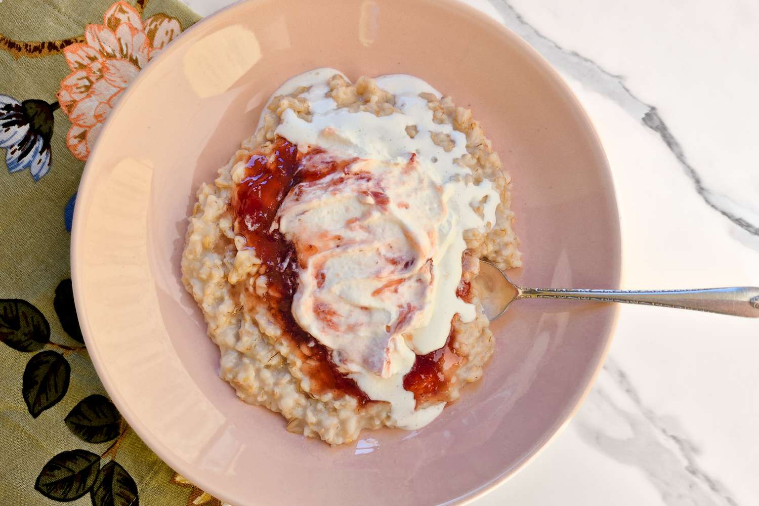 Bowl of oatmeal with cream and a fruit topping on a table with a floralthemed napkin and a spoon