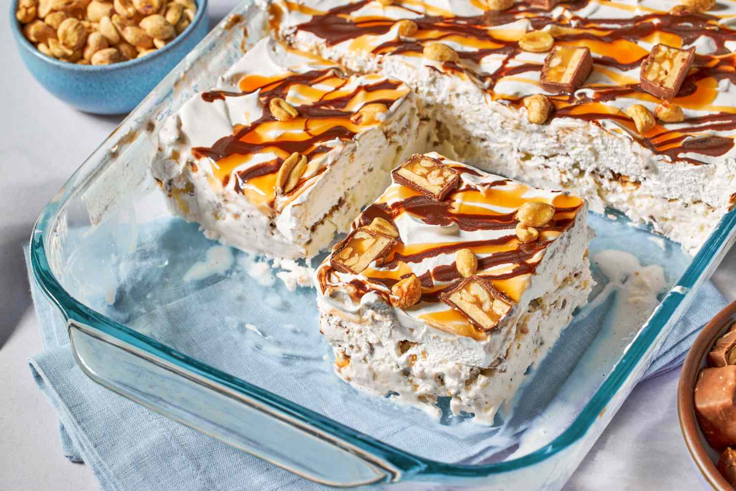 A dessert in a glass baking dish, topped with peanuts, caramel, chocolate drizzle, and candy pieces