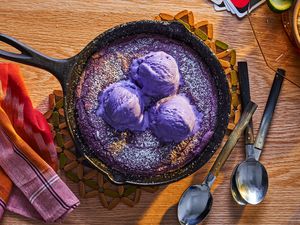 Ube skillet cookie topped with ube ice cream, spoons alongside