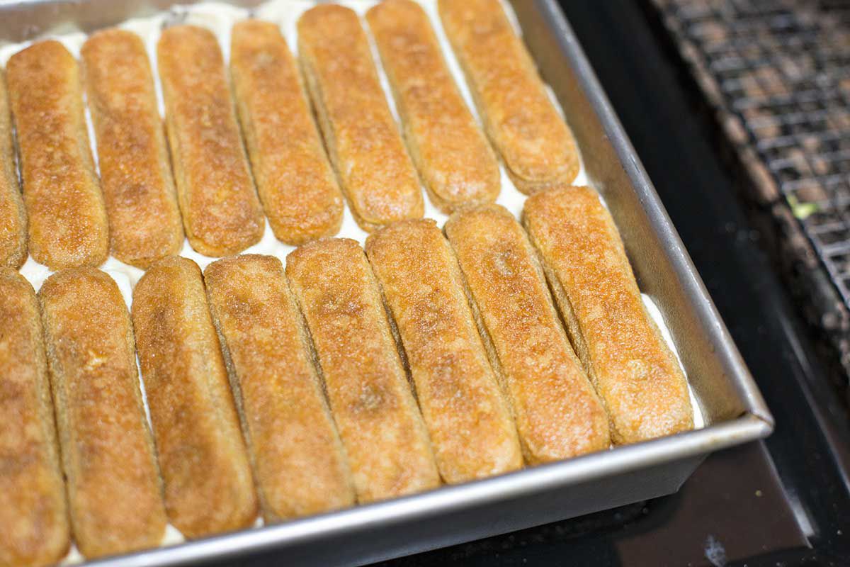 Ladyfingers lined up over tiramisu filling in a pan