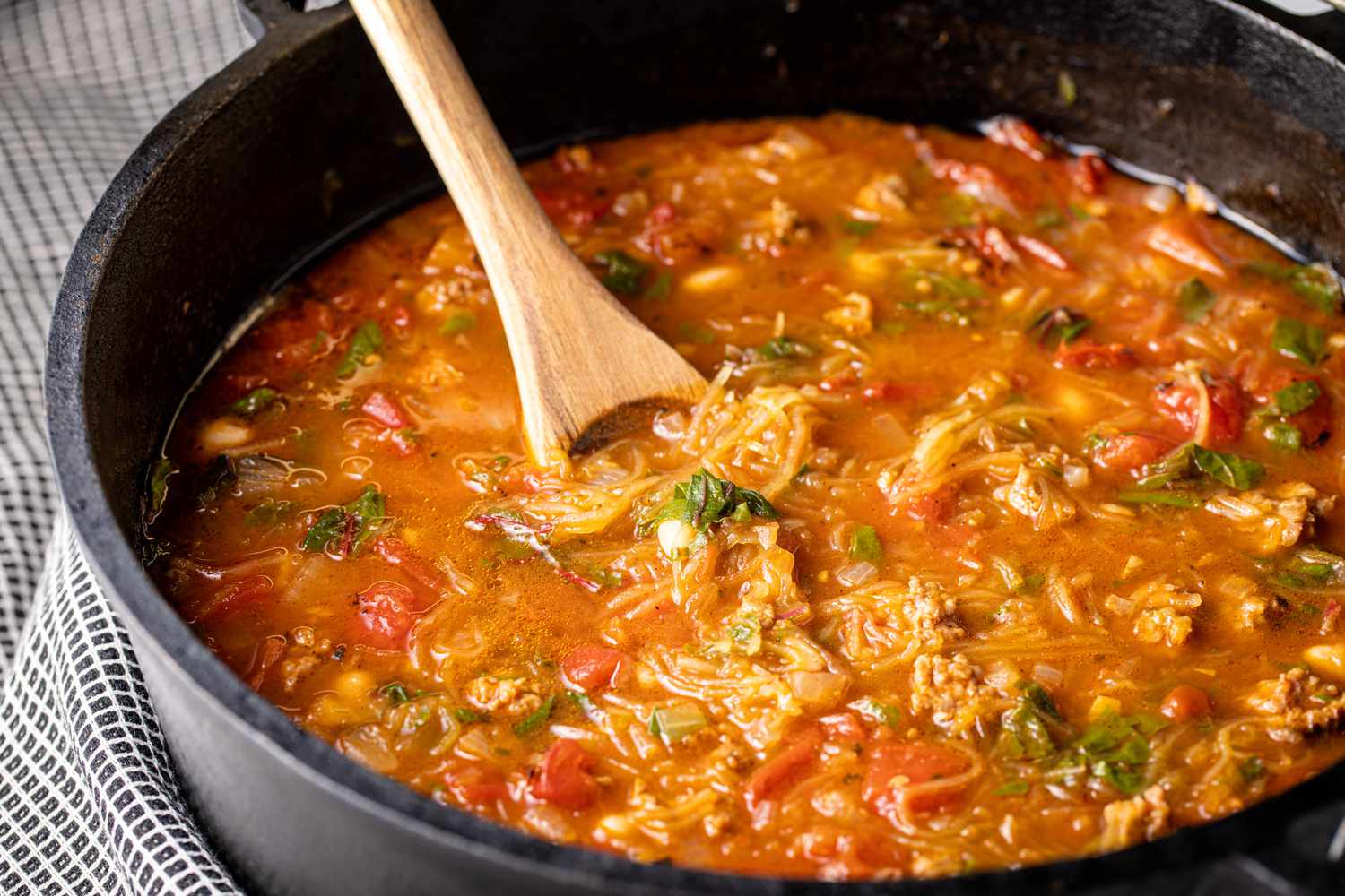 Spaghetti Squash Soup with Italian Sausage in a Cast Iron Pot with a Spoon in It Next to a Kitchen Towel