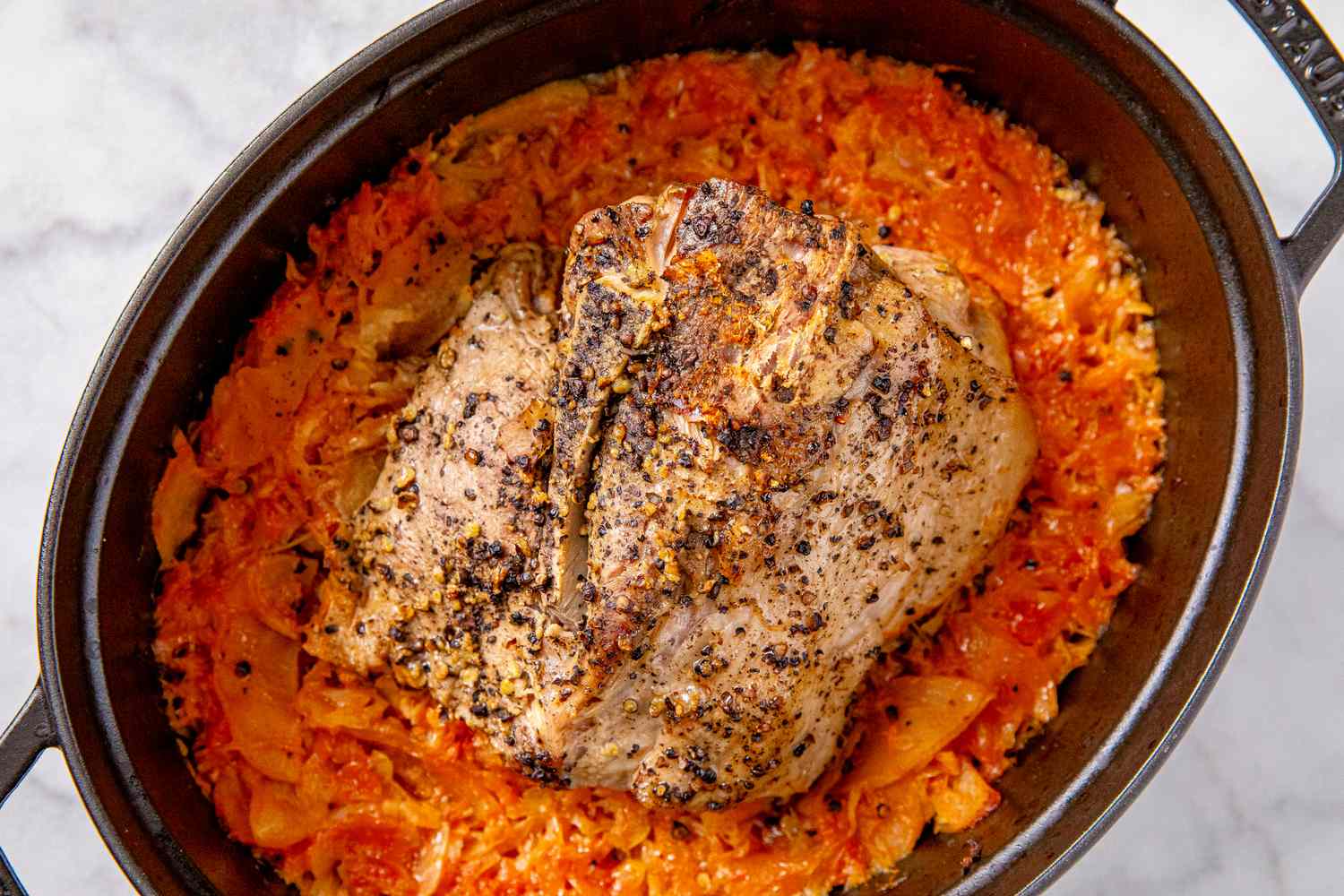 A braised pork roast placed on a bed of sauerkraut in a pot ready to serve