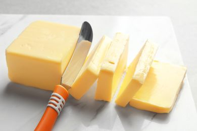 A block of butter being sliced with a knife resting on a marble surface