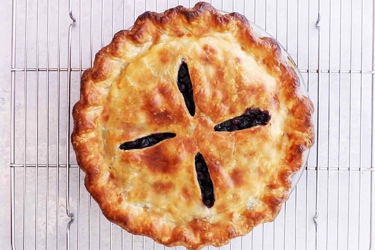 A cooked blueberry pie resting on a cooling rack