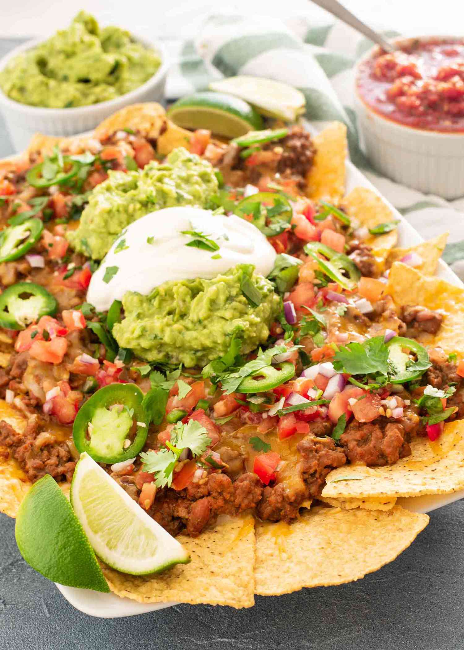 Loaded nachos topped with jalapeños, guacamole, and sour cream with a ramekin of salsa behind it 