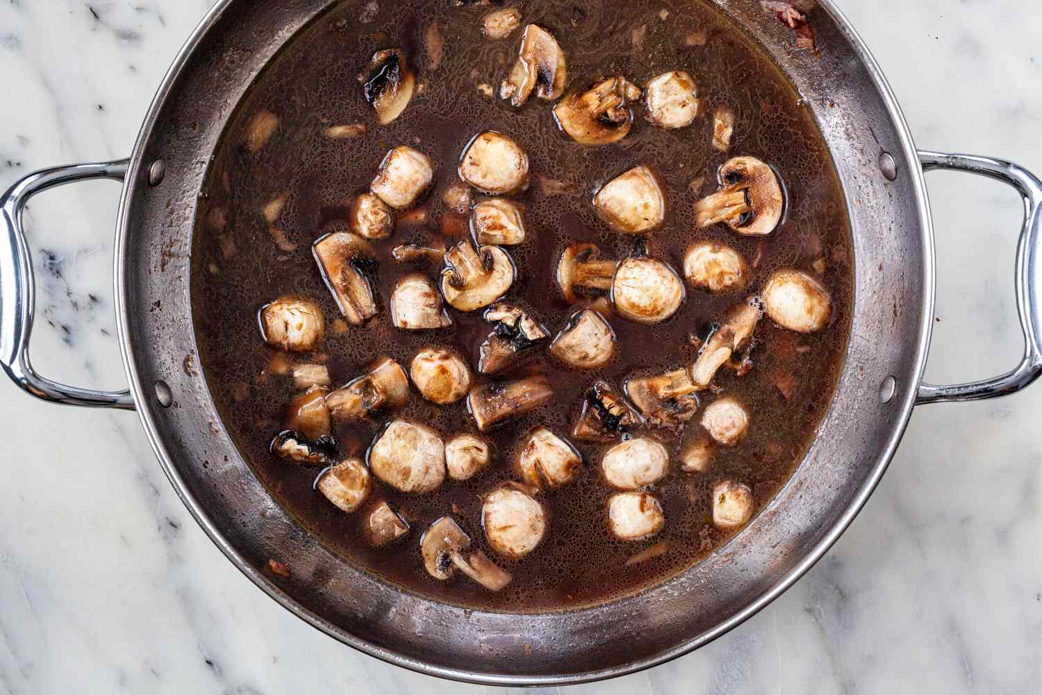Mushrooms added to a stockpot with liquid to make a coq au vin recipe.