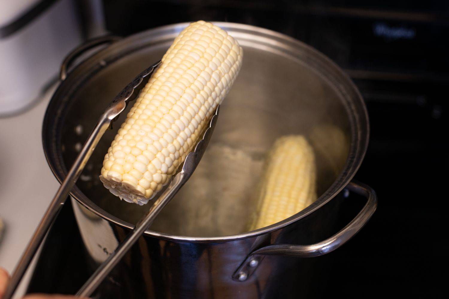 Tongs adding an ear of corn into a pot of boiling water