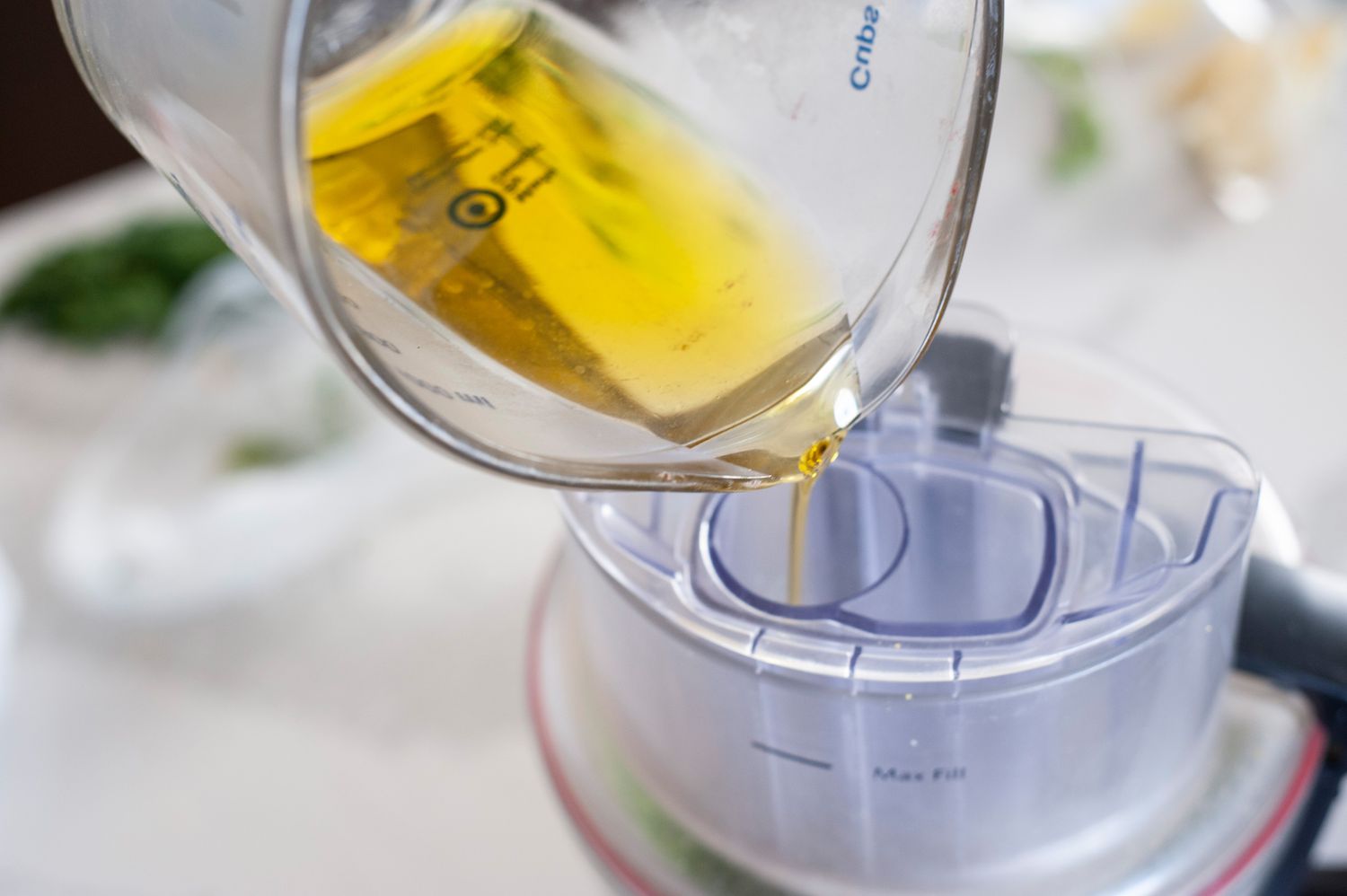 Pouring olive oil into food processor to make scallion pesto