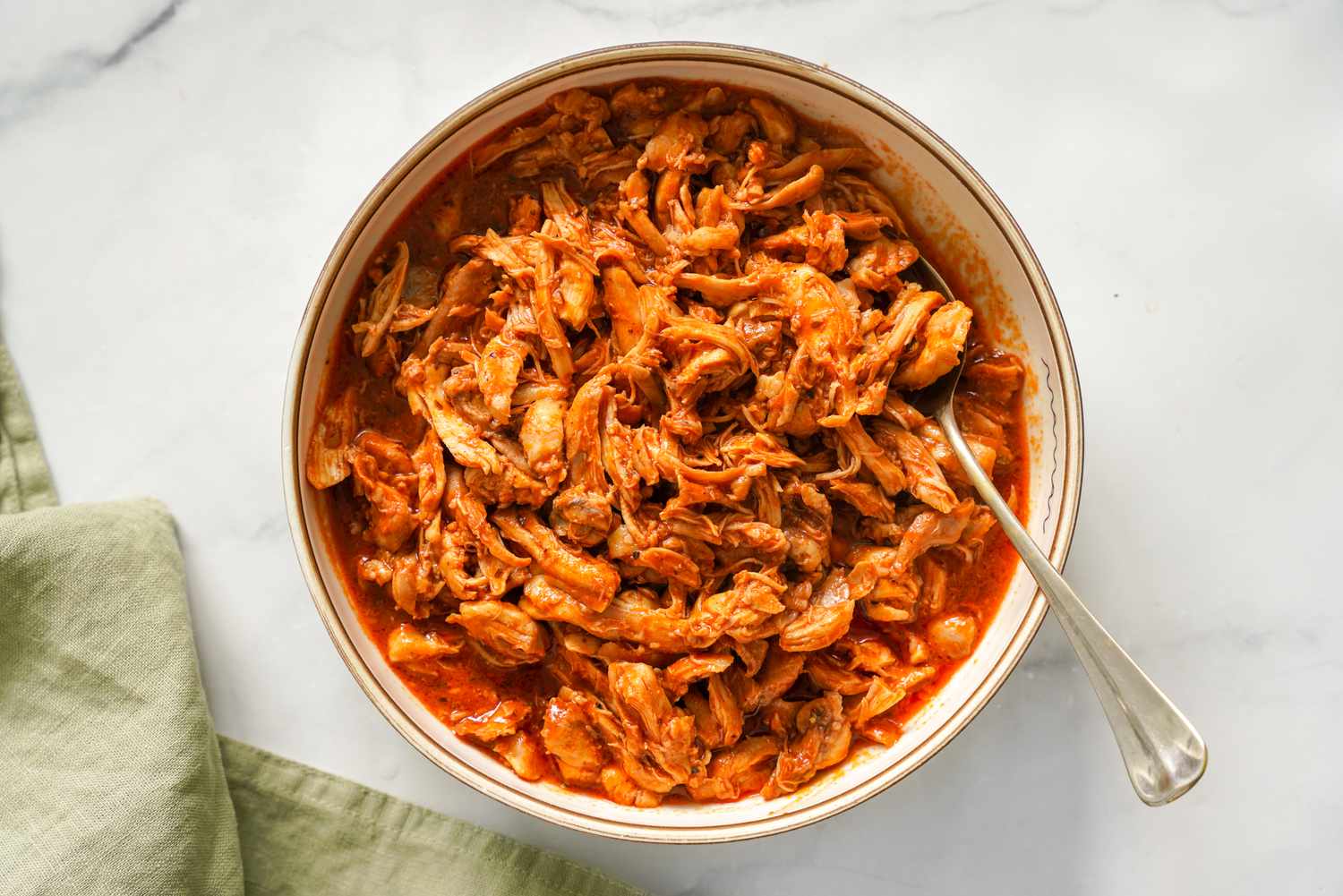 Bowl of Pulled Chicken With a Spoon and a Light Green Table Napkin