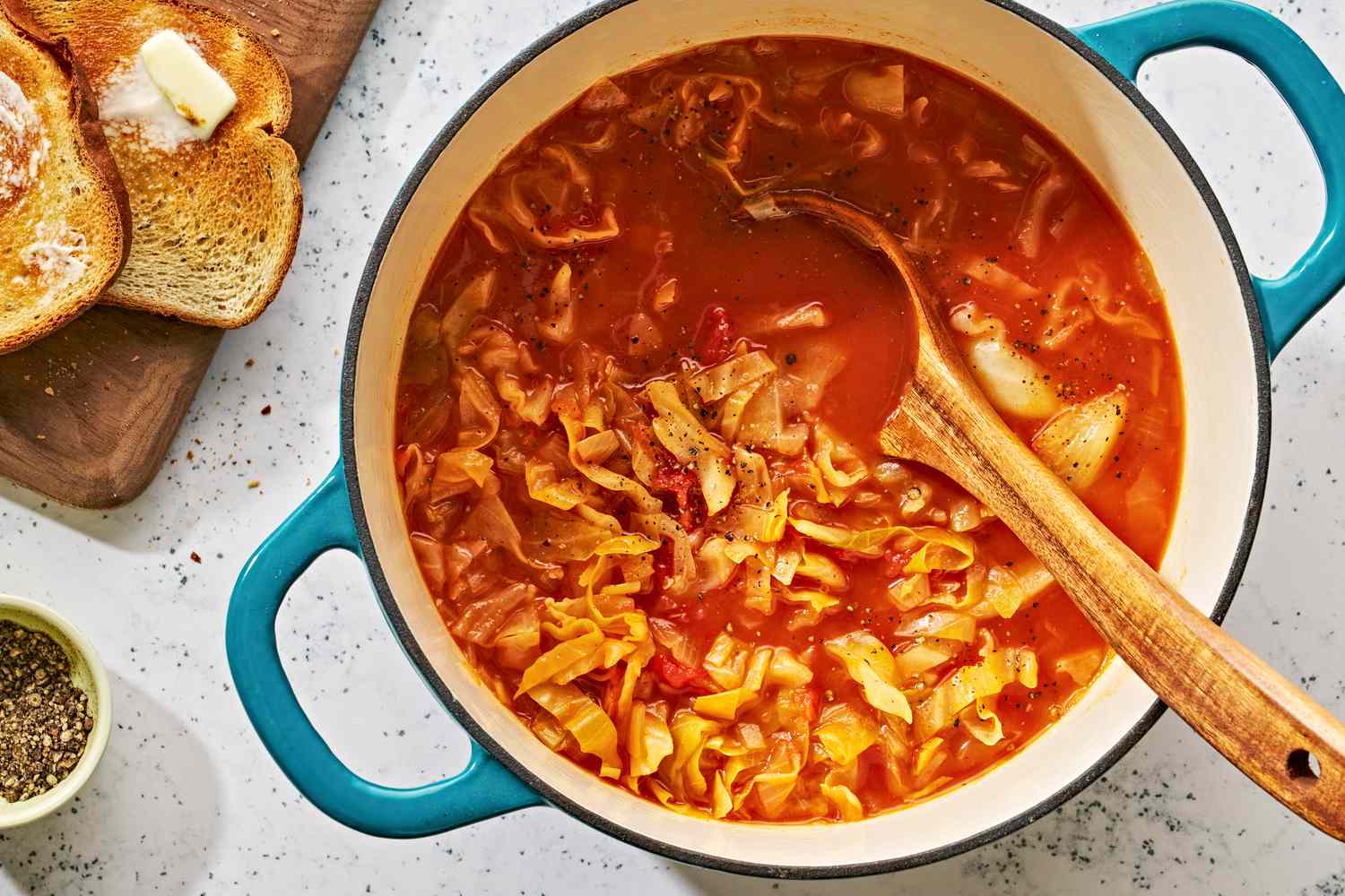 A pot of cabbage soup with wooden a spoon in it and toast on the side
