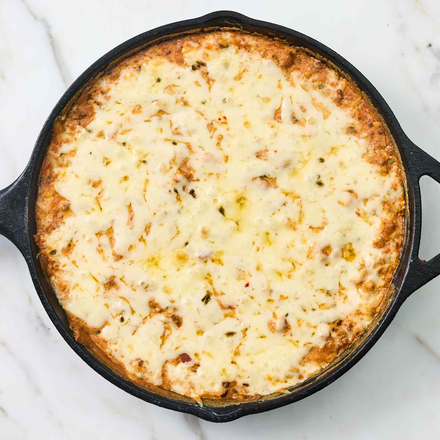 A skillet of baked dip with a melted cheese topping