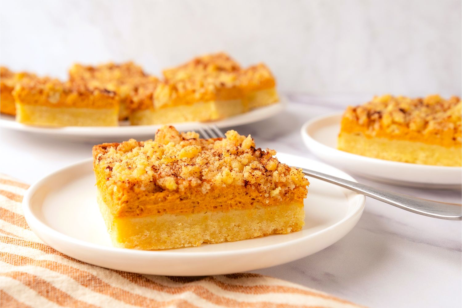 Pumpkin Cream Cheese Bars on a platter in the background, 2 plates with one bar each