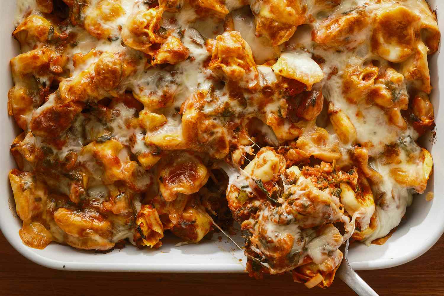 Casserole dish of tortellini casserole, serving spoon removing a cheesy spoonful