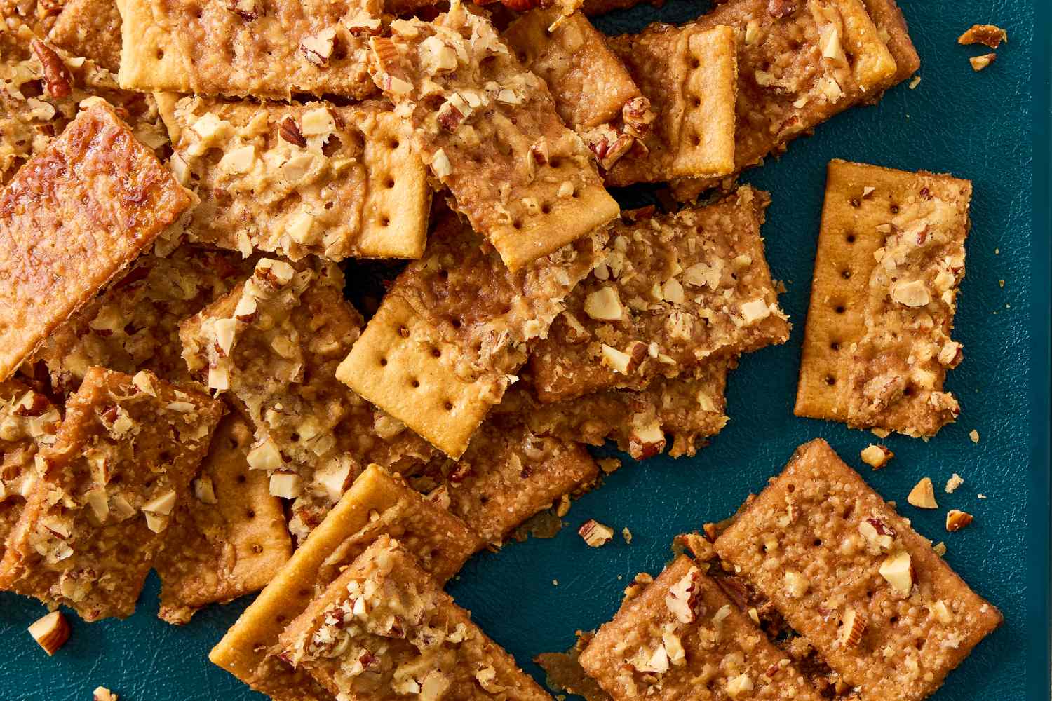A pile of club crackers topped with crushed nuts on a teal background