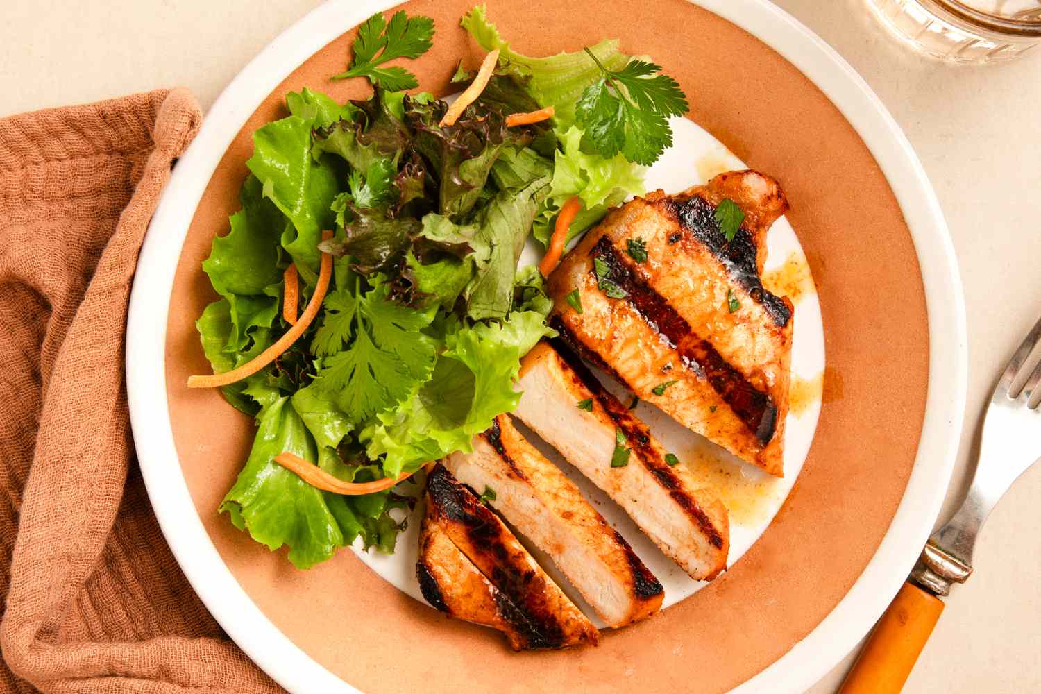 A plate with sliced pork chops with a glaze served with a side of mixed greens