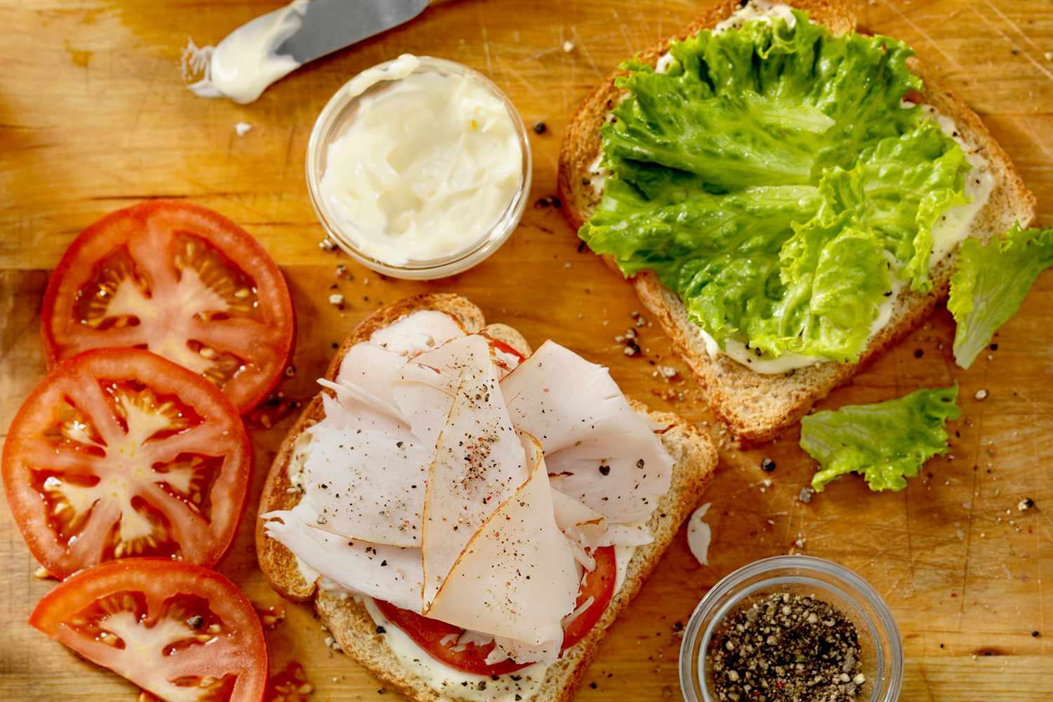 Preparation of a sandwich with lettuce sliced tomatoes turkey and black pepper