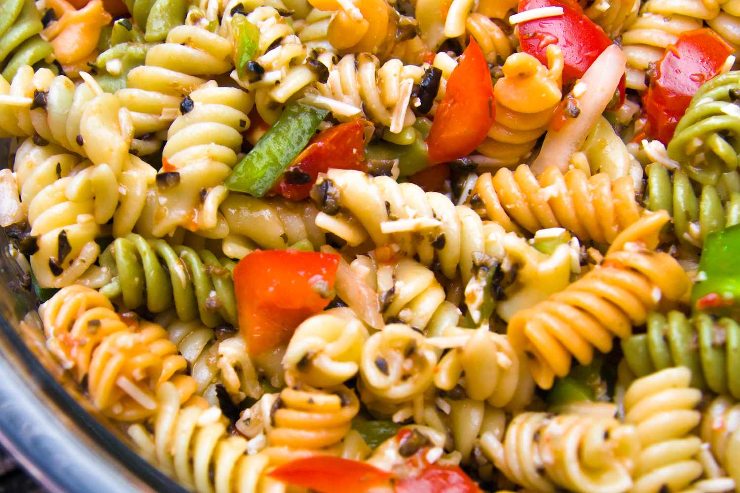 A bowl of rotini pasta salad with chopped vegetables and seasoning