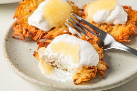 Plate of prepared latkes topped with sour cream and applesauce displaying a fork and partially eaten piece