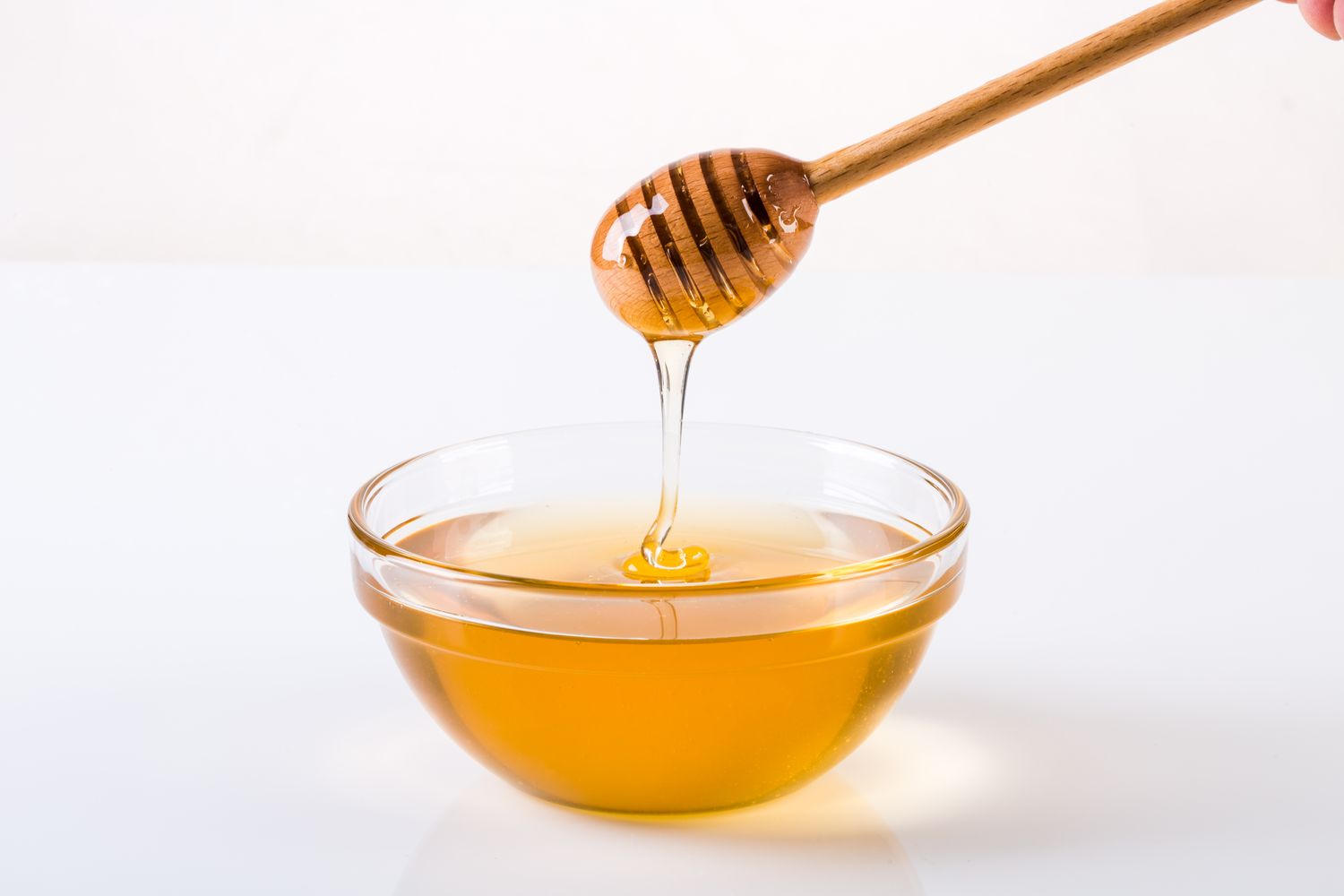 Honey dripping from a dipper into a clear bowl of honey