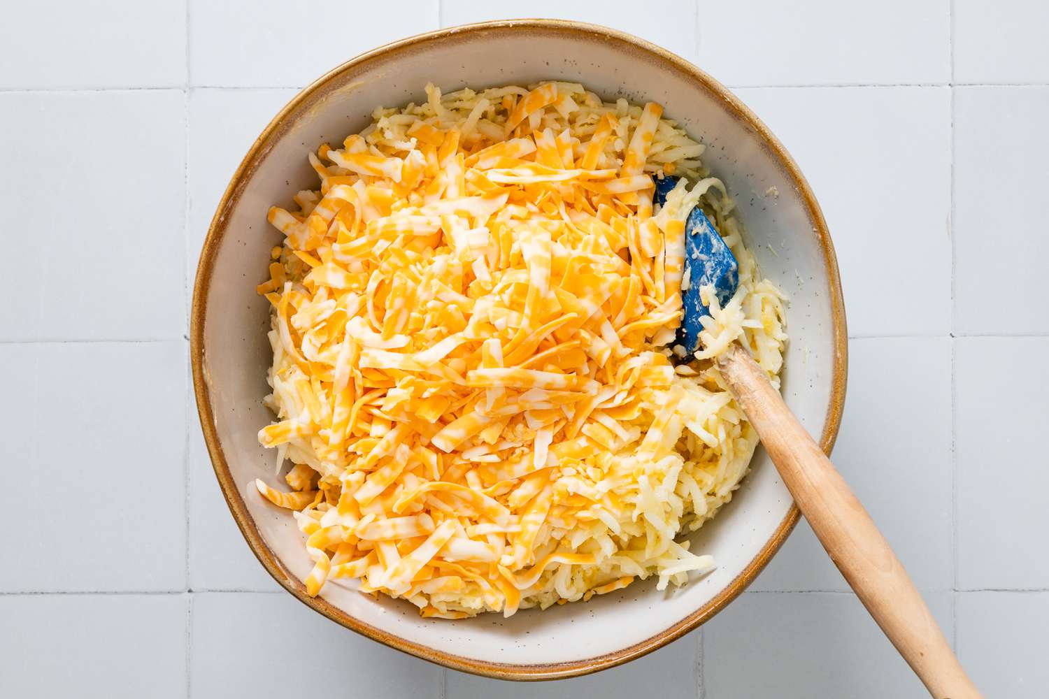 Shredded cheese added to bowl of copycat Cracker Barrel hash brown casserole ingredients