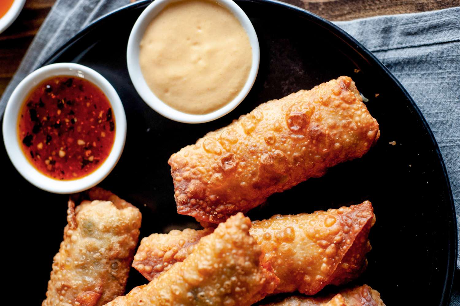 A dark plate with stacked vegetable egg rolls and dipping sauce