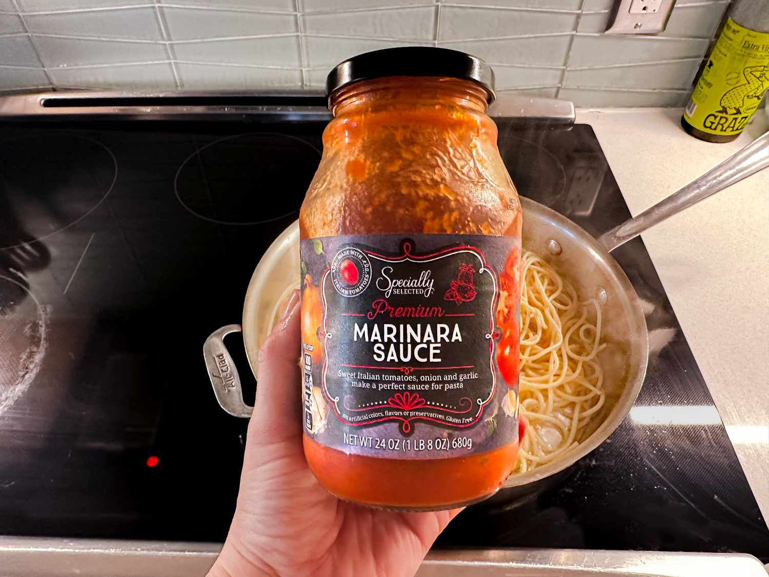 someone holding up a jar of specially selected marinara sauce over a skillet of cooked pasta